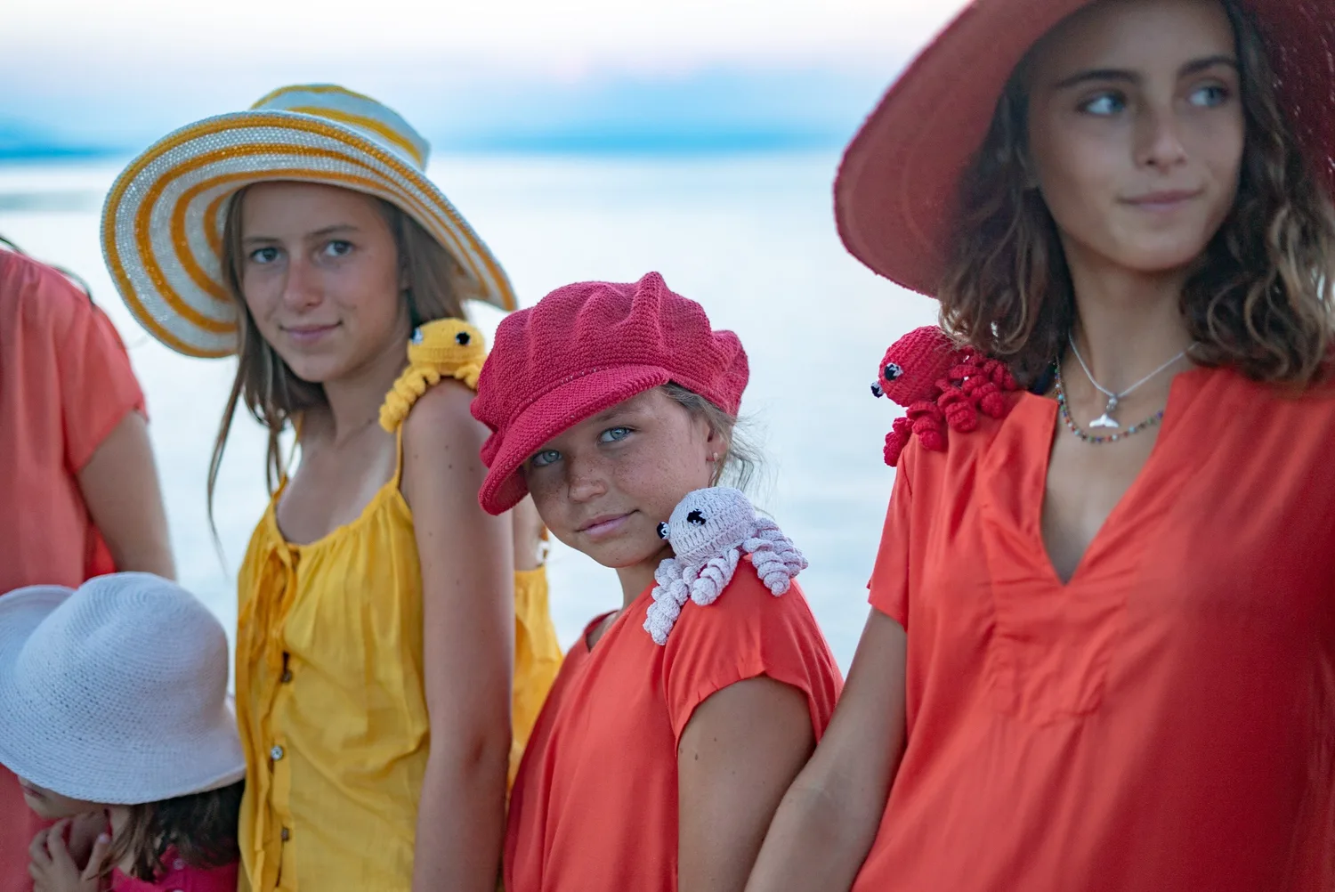 Jeunes filles en tuniques corail et jaune, chapeaux et pieuvres crochetées devant la mer pâle à Porquerolles.
