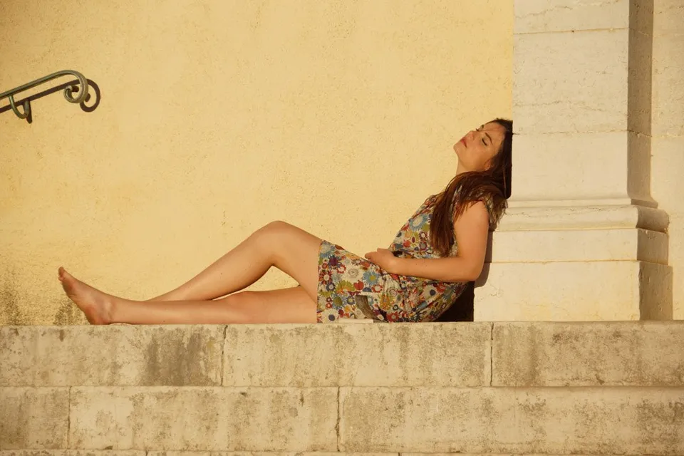 Femme en robe fleurie assise sur des marches de pierre contre un mur jaune, lumière dorée à Porquerolles.
