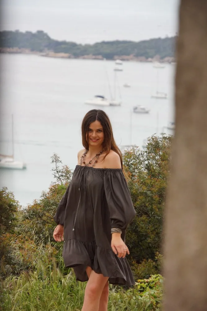 Femme en robe gris anthracite à épaules dénudées, devant une baie et des bateaux à voile à Porquerolles.
