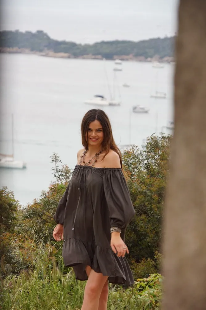 Femme en robe gris anthracite à épaules dénudées, devant une baie et des bateaux à voile à Porquerolles.
