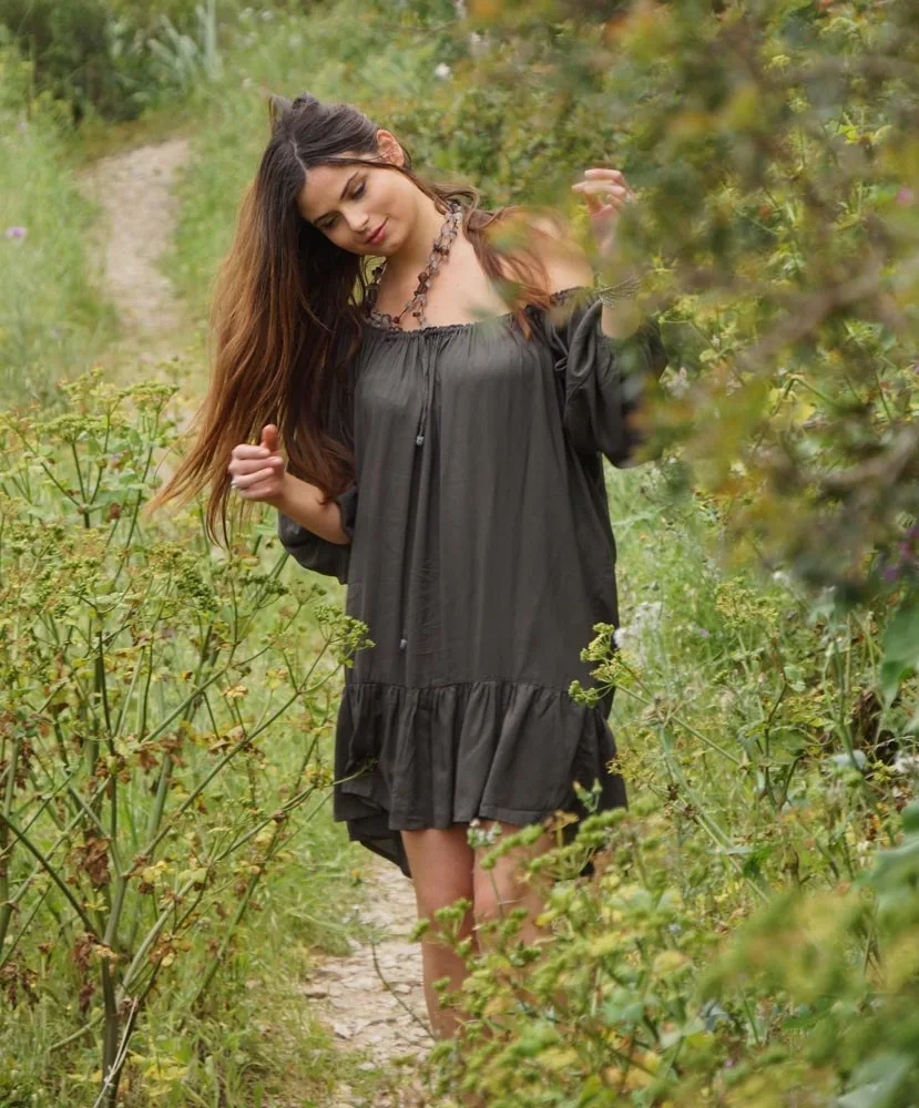 Femme en robe grise à épaules nues marche dans un chemin de fleurs sauvages du maquis à Porquerolles.