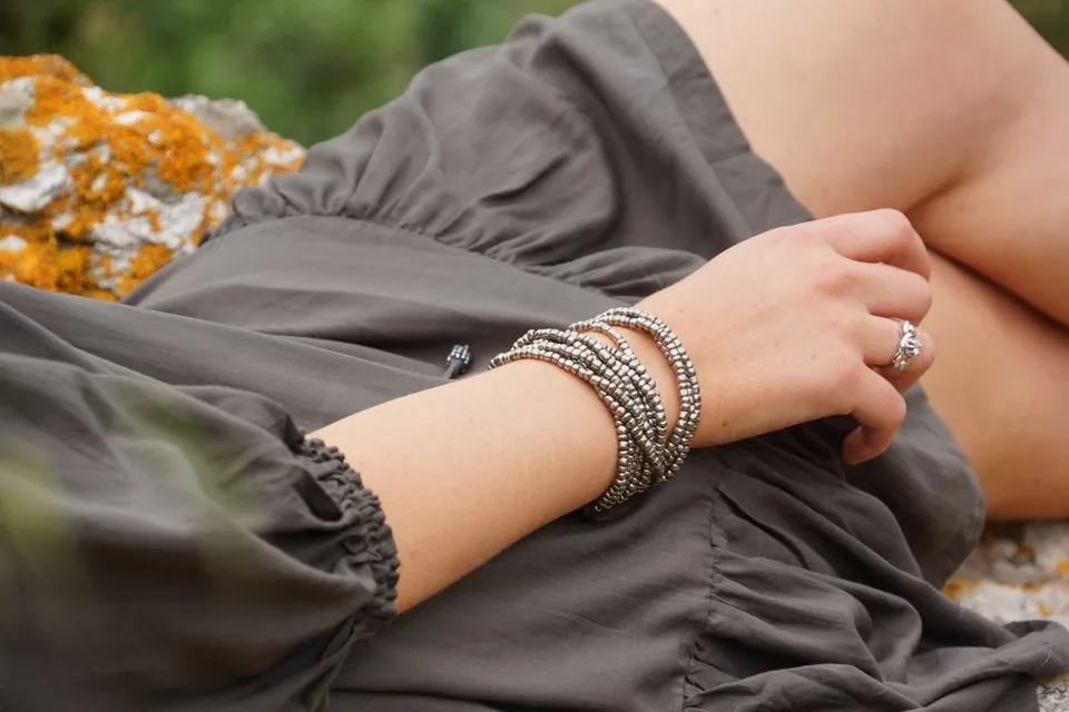 Bras posé sur une robe olive, large bracelet et bague d'argent, roche orangée de lichen, à Porquerolles.