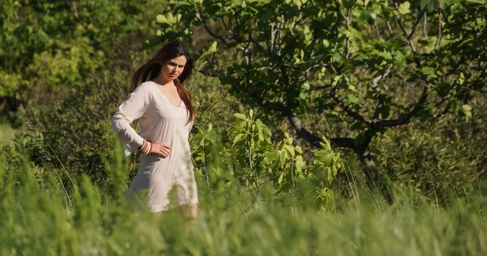 Femme en tunique claire marchant dans l'herbe haute près d'un figuier du maquis ensoleillé à Porquerolles.