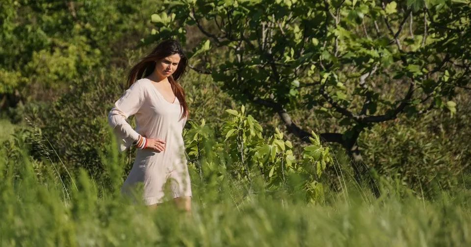 Femme en tunique claire marchant dans l'herbe haute près d'un figuier du maquis ensoleillé à Porquerolles.