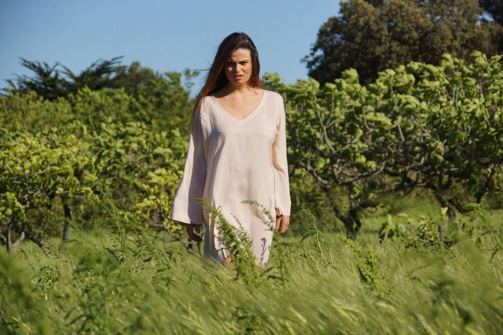Femme en tunique rose pâle à manches longues, debout dans les hautes herbes du maquis à Porquerolles.