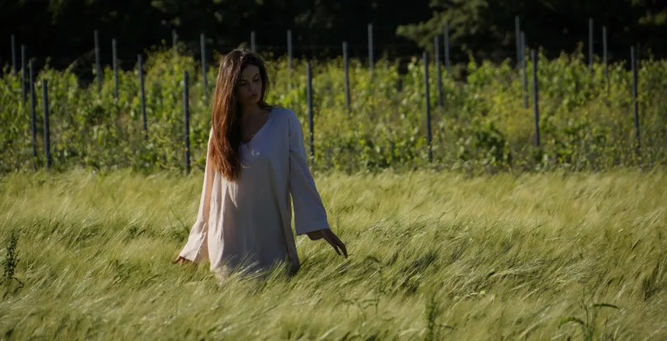 Femme en tunique crème marchant dans un champ de céréales en contre-jour doré à Porquerolles.