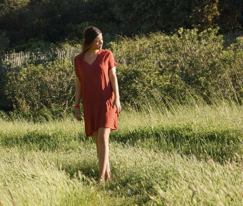 Femme en robe terracotta marchant dans les herbes hautes sous la lumière dorée à Porquerolles.