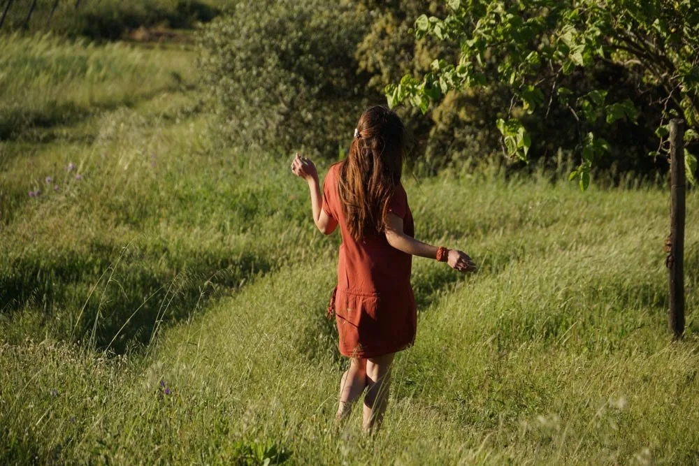Femme vue de dos en robe terracotta marchant dans une prairie d'herbes hautes à l'heure dorée à Porquerolles.