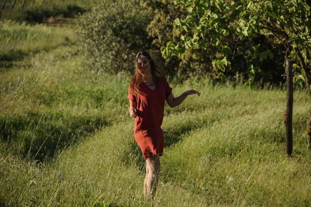Femme en robe terracotta dans une prairie d'herbes hautes, maquis en arrière-plan sous lumière dorée à Porquerolles.