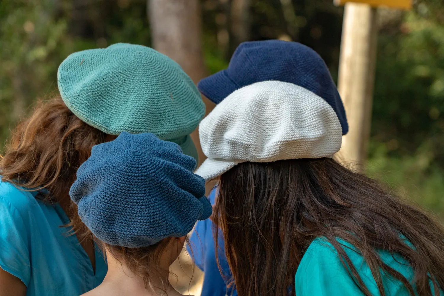 Trois enfants de dos en hauts turquoise et bonnets au crochet menthe, marine et écru, à Porquerolles.