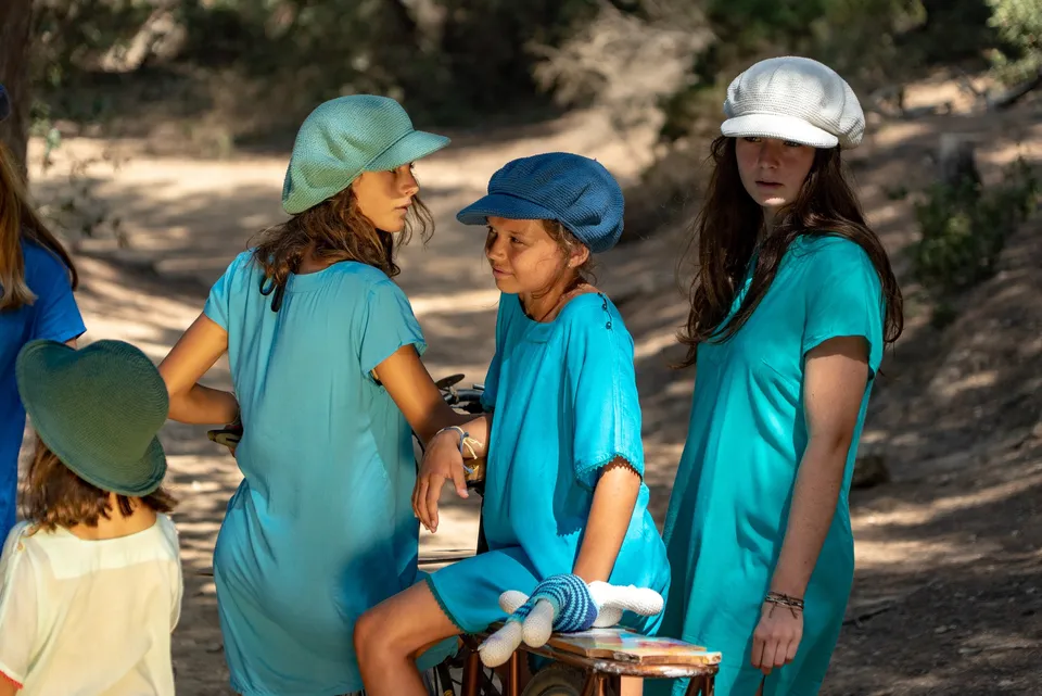 Trois enfants en robes turquoise et casquettes autour d'un vélo, lapin en crochet sur le porte-bagages à Porquerolles.