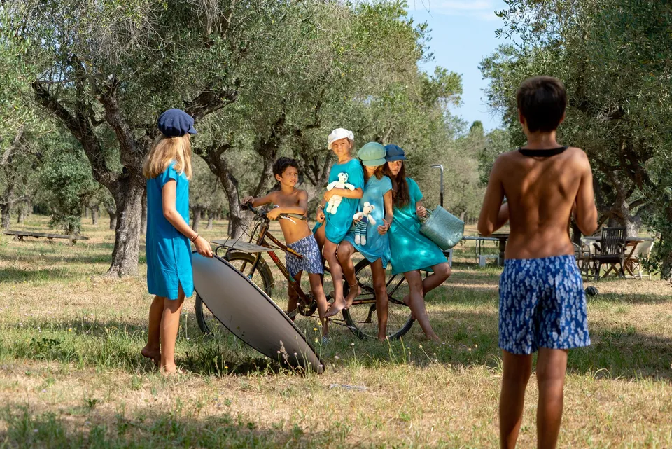Groupe d'enfants en tuniques bleues et chapeaux posant avec un vélo parmi les oliviers à Porquerolles.