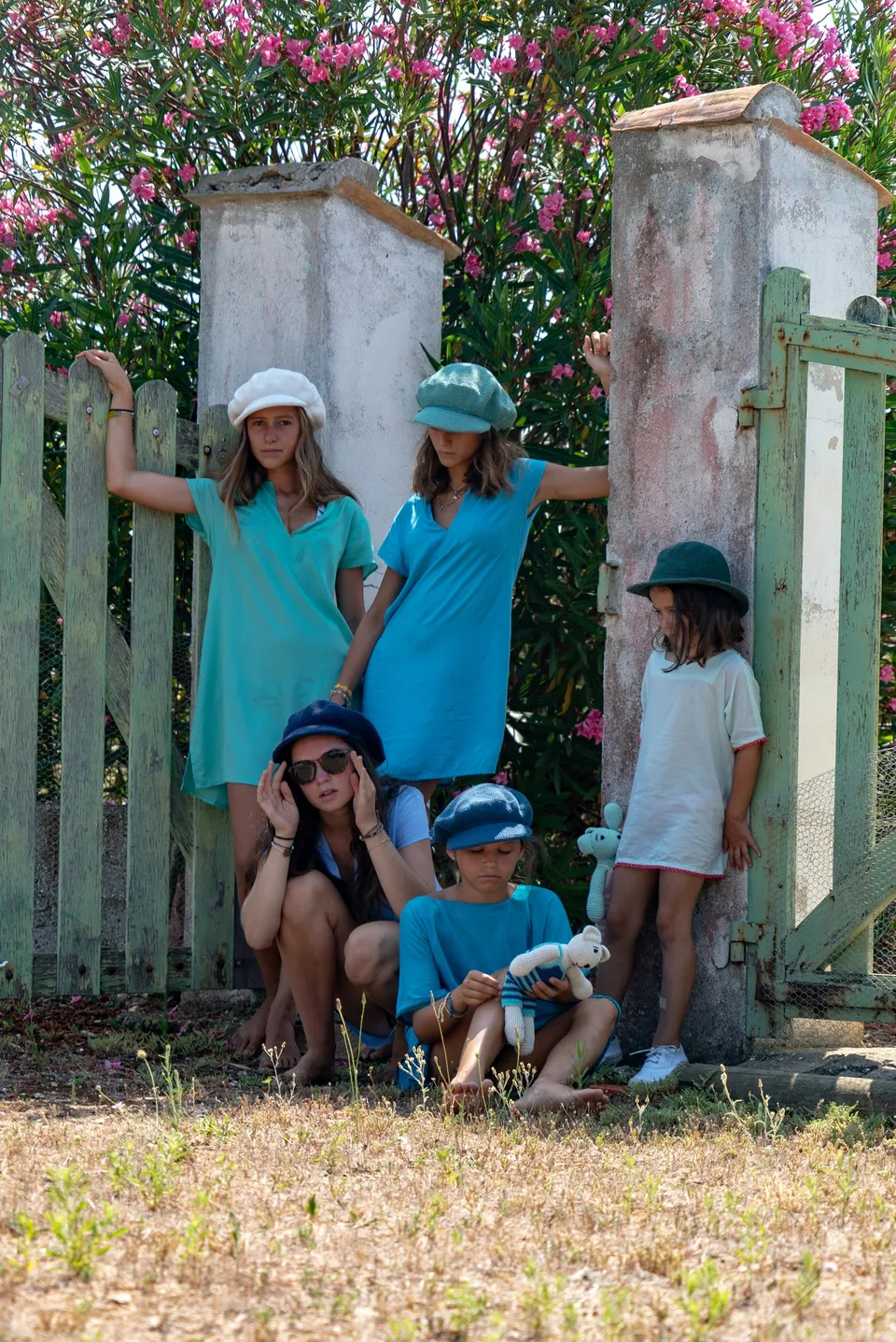 Jeunes en tuniques bleues et chapeaux devant un portail de bois entouré de lauriers-roses à Porquerolles.