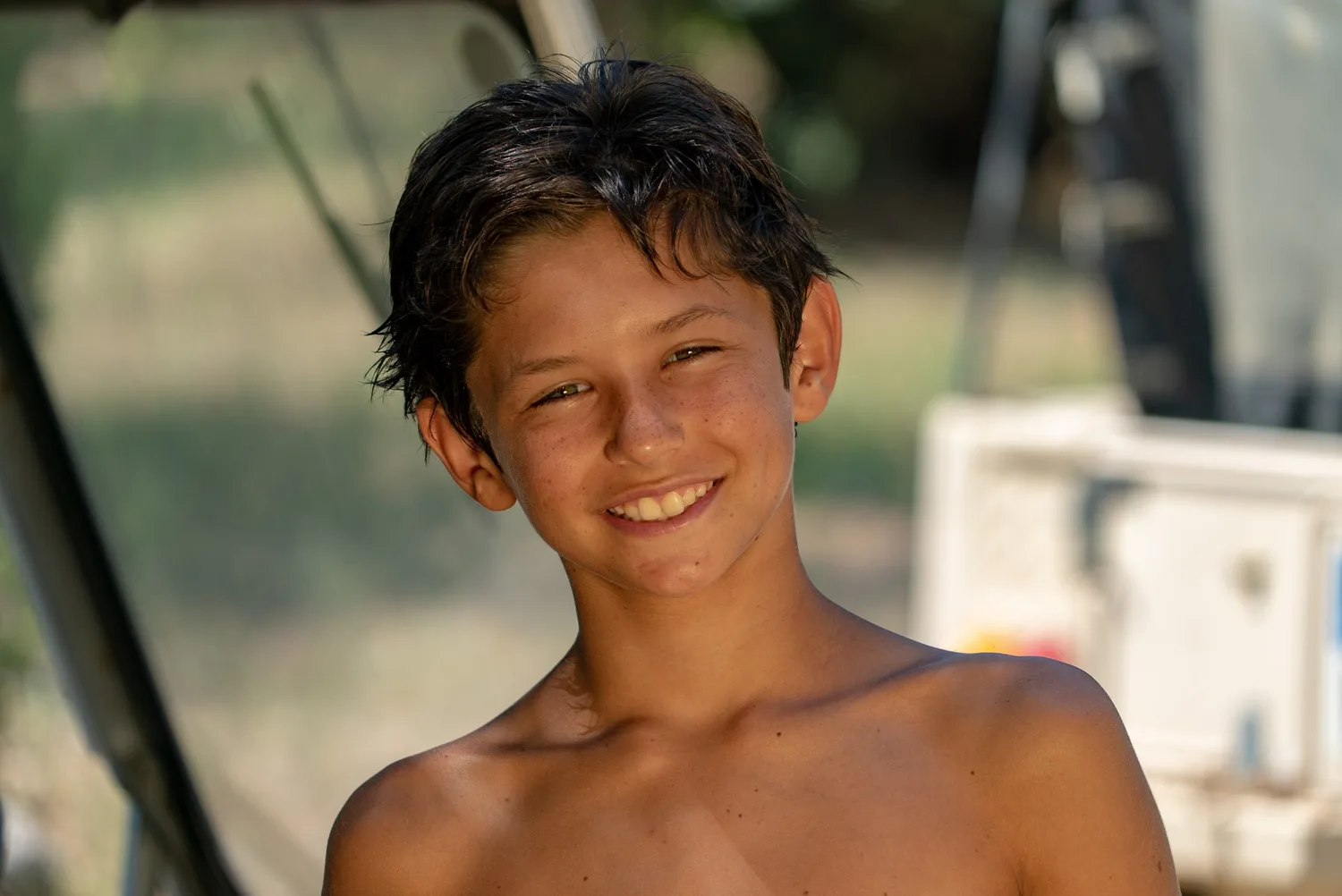 Garçon torse nu aux cheveux mouillés souriant à bord d'un bateau, à Porquerolles.