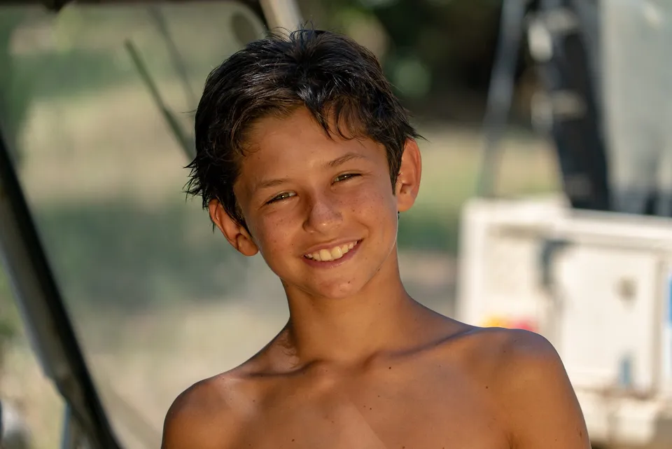 Garçon torse nu aux cheveux mouillés souriant à bord d'un bateau, à Porquerolles.
