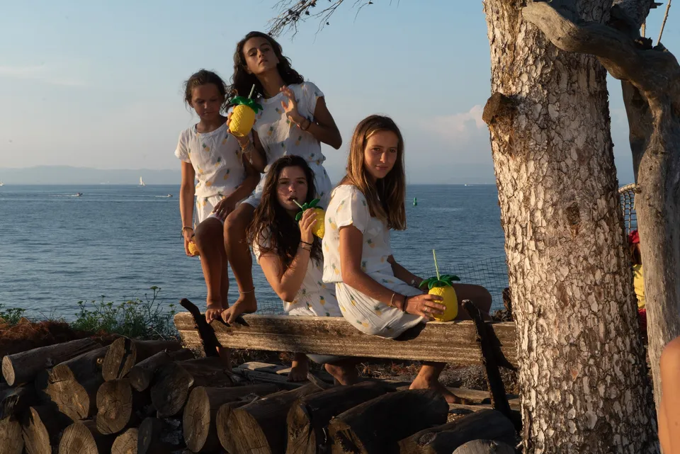 Quatre jeunes filles en robes blanches à ananas avec gobelets ludiques sur la côte au soleil doré à Porquerolles.