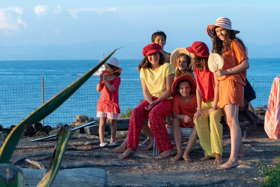 Enfants en tenues rouge jaune et orange, chapeaux de paille, terrasse face à la mer à Porquerolles.