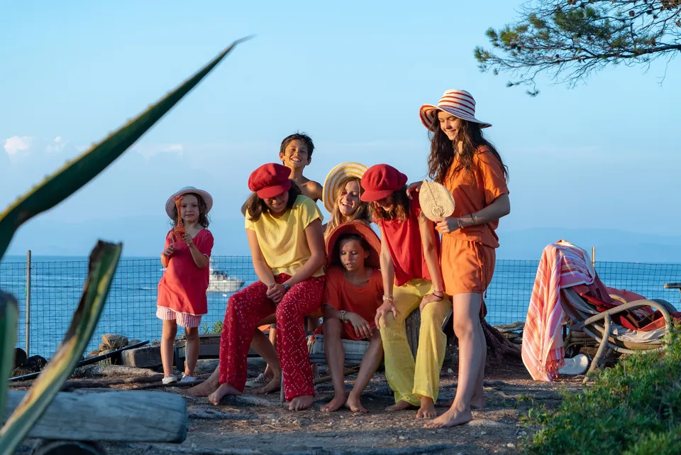 Groupe d'enfants en vêtements rouge jaune et orange avec chapeaux, sur une terrasse face à la mer à Porquerolles.