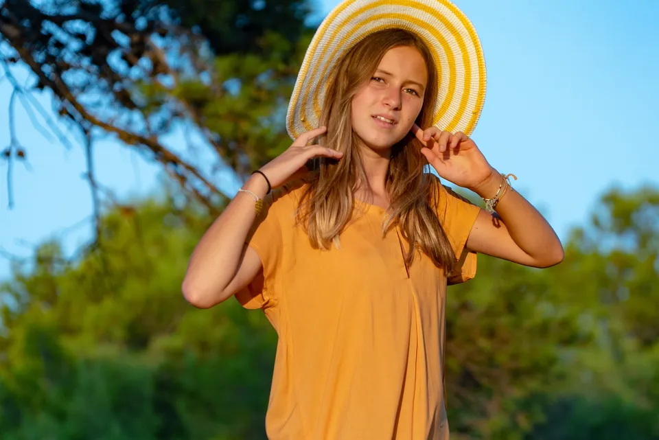 Adolescente en tunique orange et chapeau de paille rayé jaune et blanc, dans le maquis de Porquerolles.