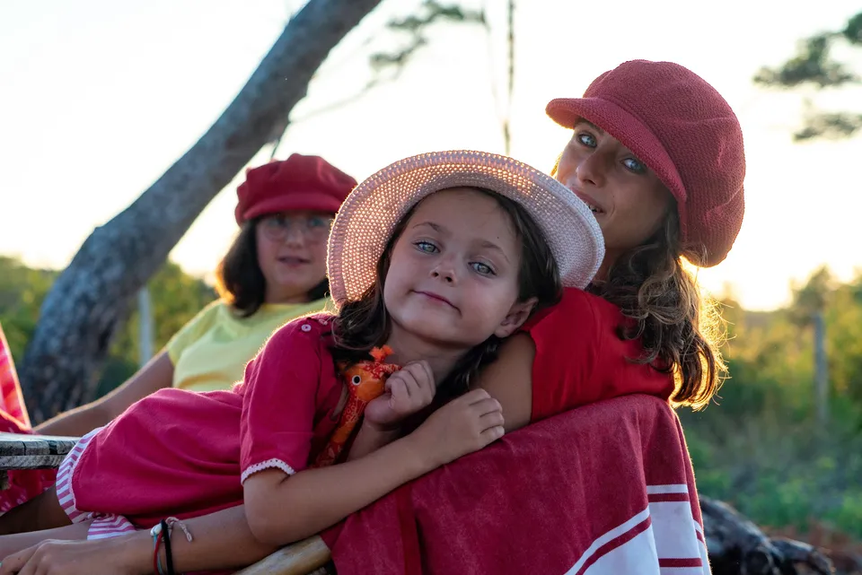 Femme et deux enfants en chapeaux rouges et paille, blottis au contre-jour doré à Porquerolles.