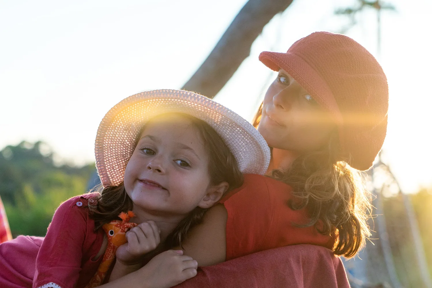 Femme et petite fille blotties, chapeau clair et bonnet terracotta, lumière dorée du soir à Porquerolles.