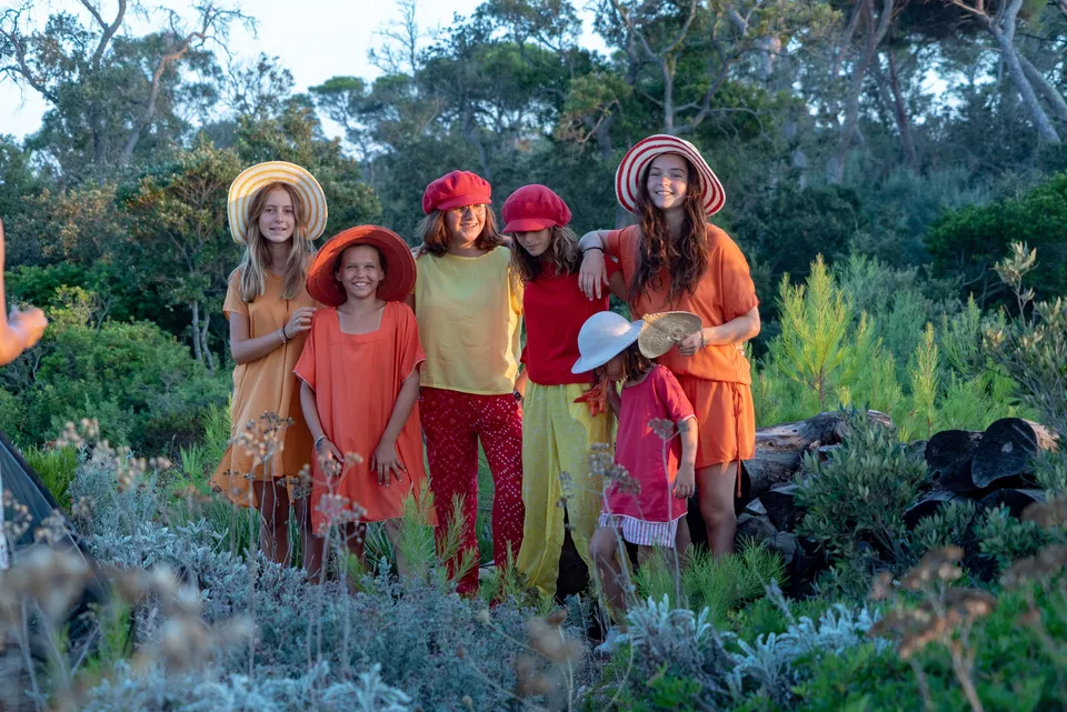 Groupe d'enfants et adolescentes en robes jaune orange et rouge, chapeaux larges dans le maquis à Porquerolles.