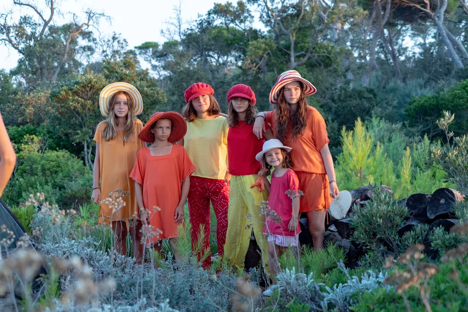 Six filles en tenues rouge orange et jaune, chapeaux assortis alignées dans le maquis doré à Porquerolles.