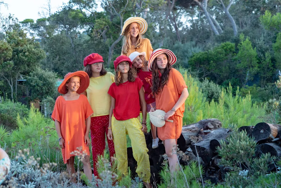Six enfants en tuniques rouge orange et jaune, chapeaux variés, posant dans le maquis de Porquerolles.