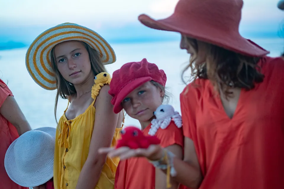 Trois jeunes filles en tuniques jaune et rouge, chapeaux et pieuvres au crochet, mer au crépuscule à Porquerolles.