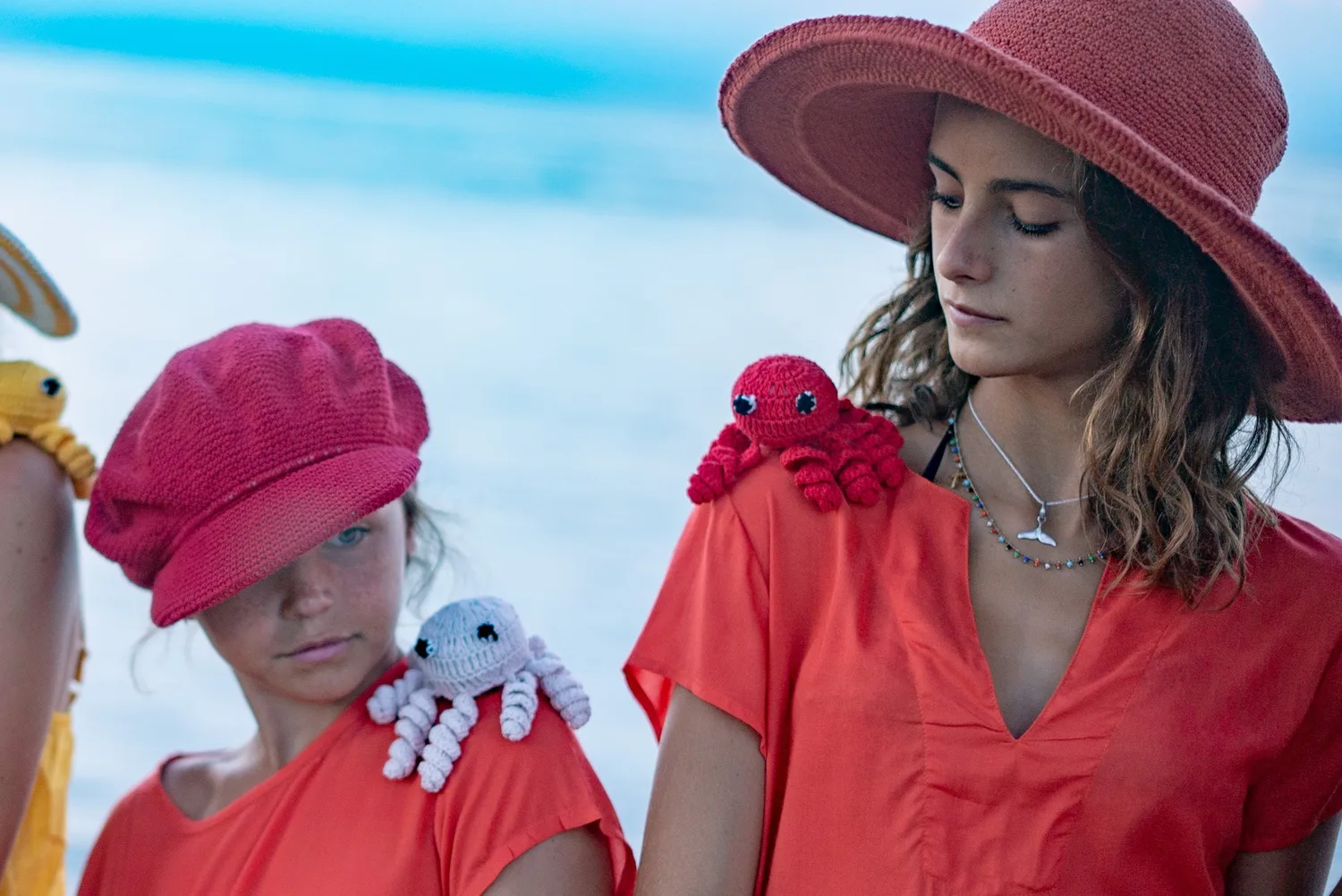 Femme et enfant en tuniques corail, chapeaux et pieuvres crochetées devant la mer à Porquerolles.