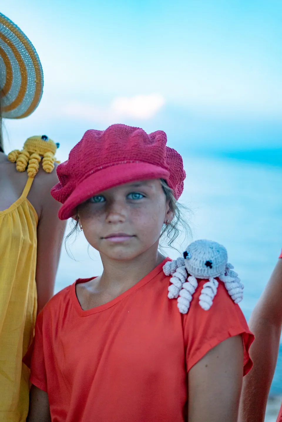 Portrait d'une fillette en casquette rouge, pieuvre crochetée sur l'épaule, mer floue derrière à Porquerolles.