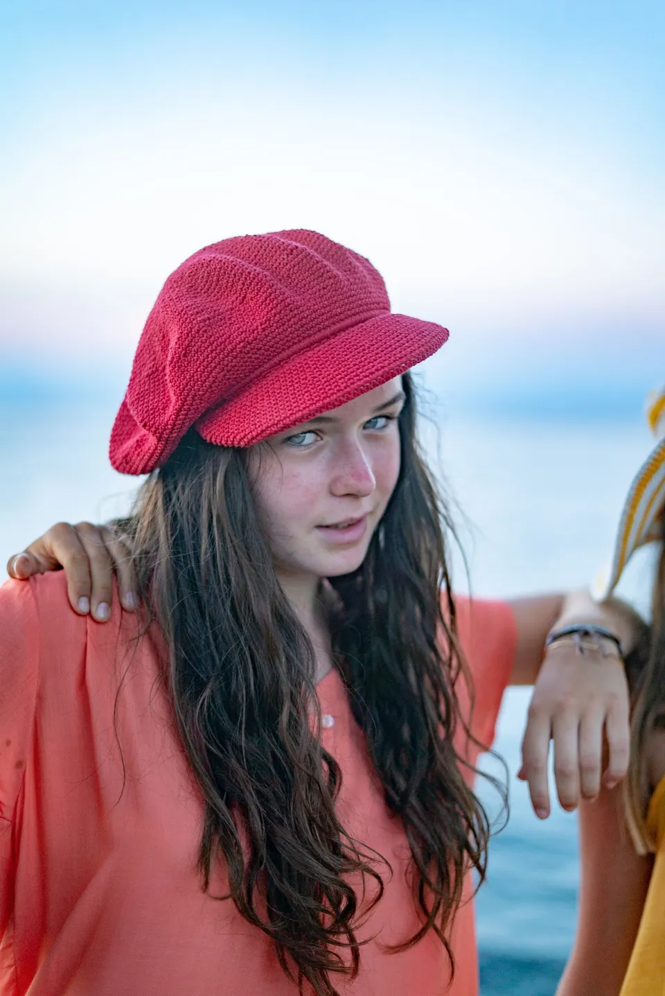 Gros plan d'une jeune fille en casquette rouge au crochet et blouse corail, mer derrière à Porquerolles.