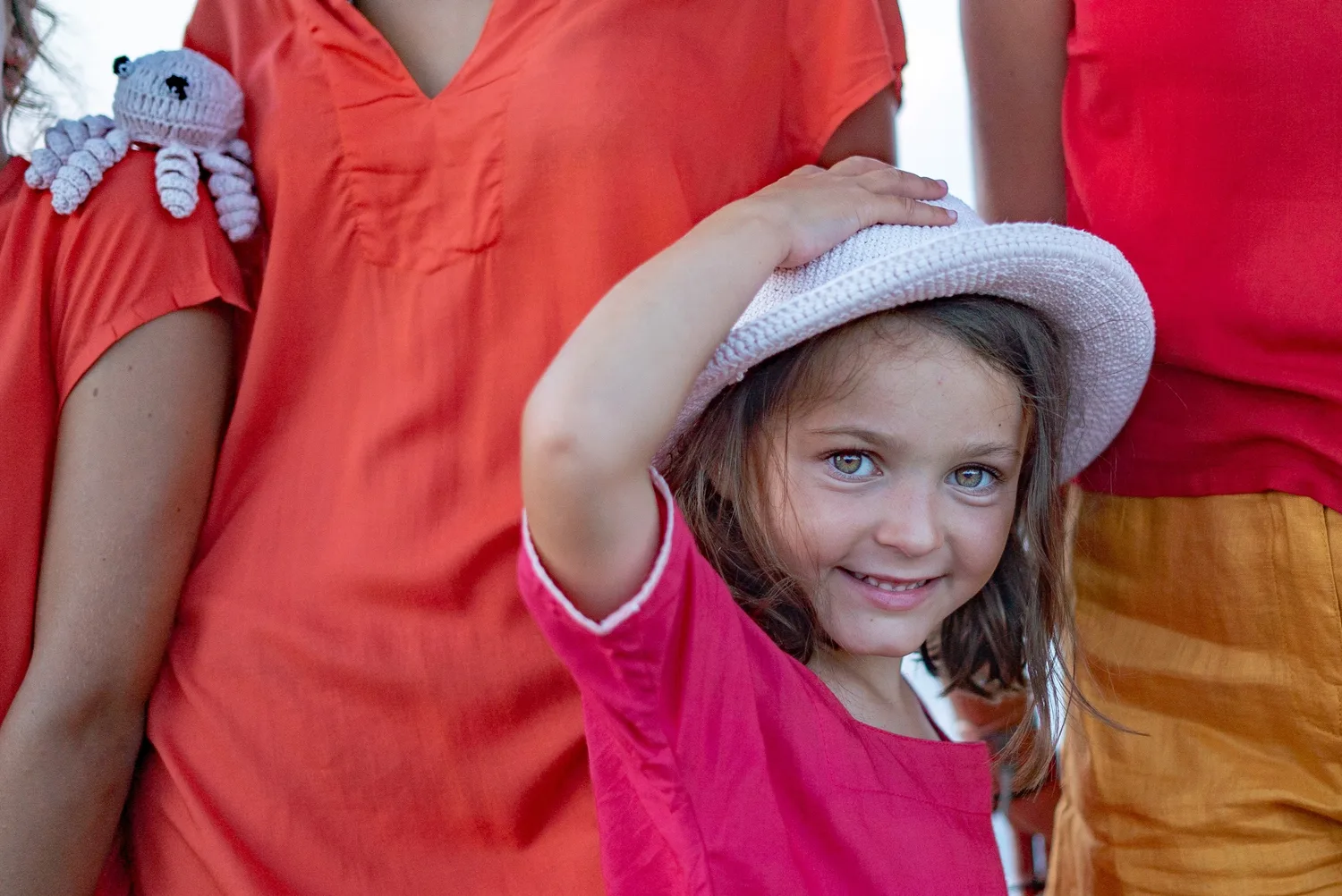 Fille en tunique rose-rouge et chapeau de crochet blanc, pieuvre blanche au crochet, lumière douce à Porquerolles.