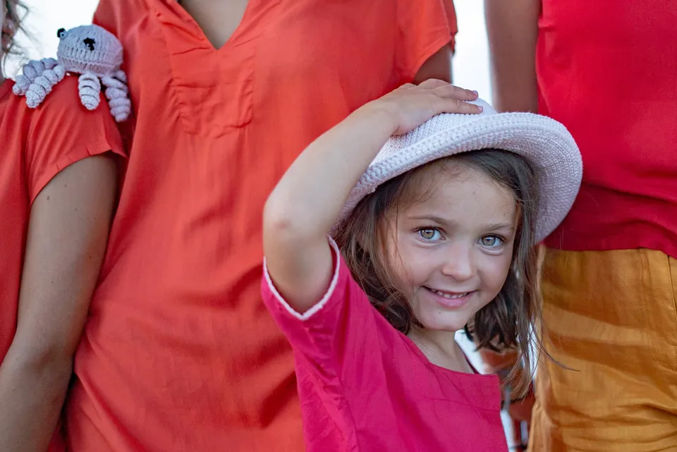 Fille en tunique rose-rouge et chapeau de crochet blanc, pieuvre blanche au crochet, lumière douce à Porquerolles.