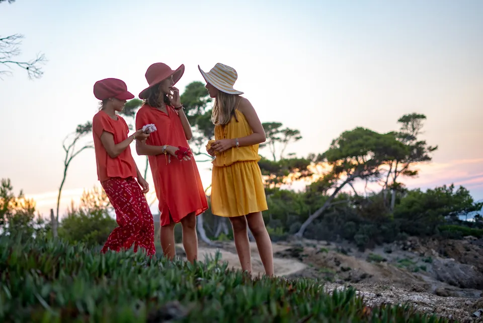Trois jeunes en rouge et jaune, chapeaux assortis sur un sentier côtier au crépuscule à Porquerolles.