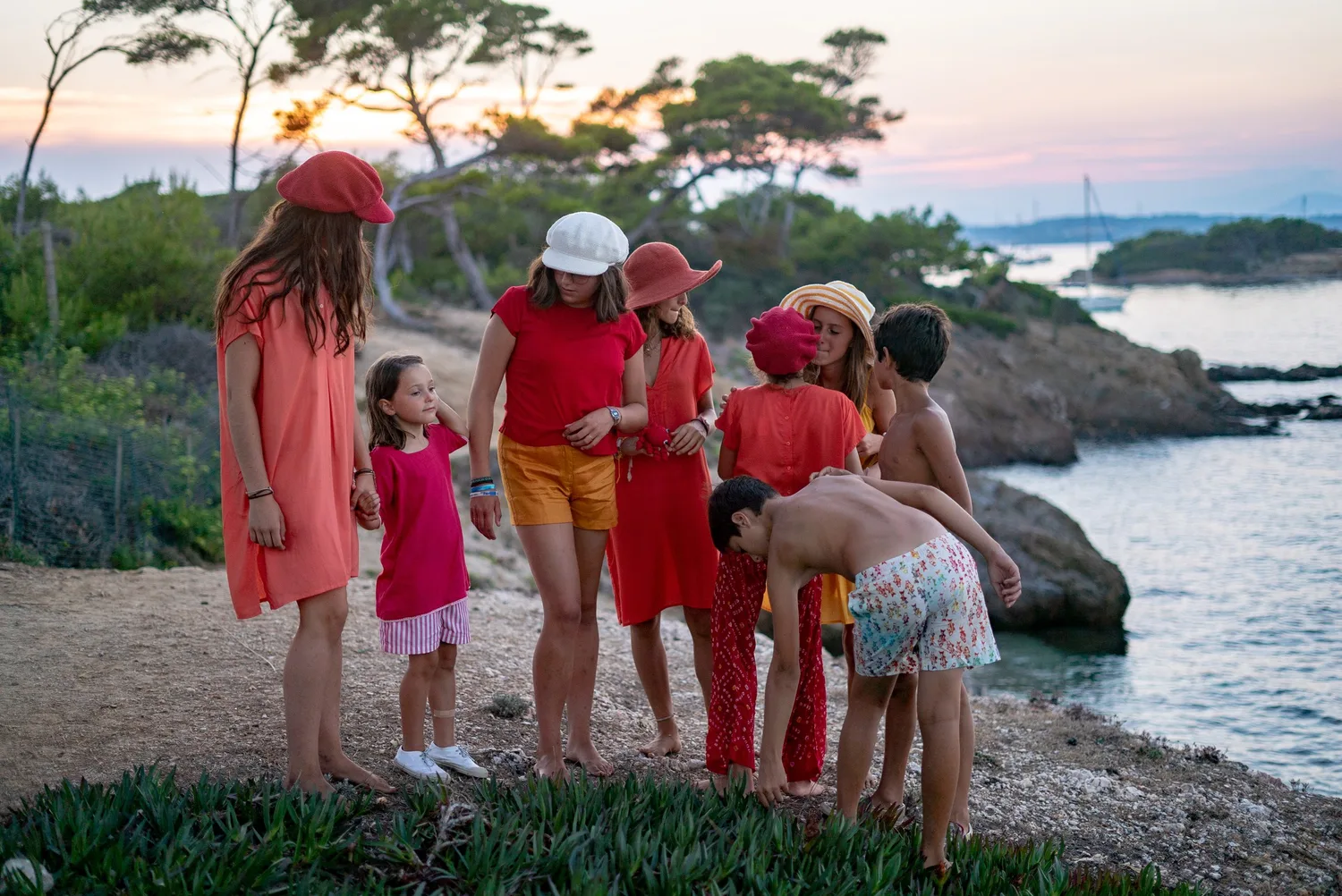 Groupe d'enfants en tenues rouge et orange sur un sentier côtier au crépuscule face à la mer à Porquerolles.