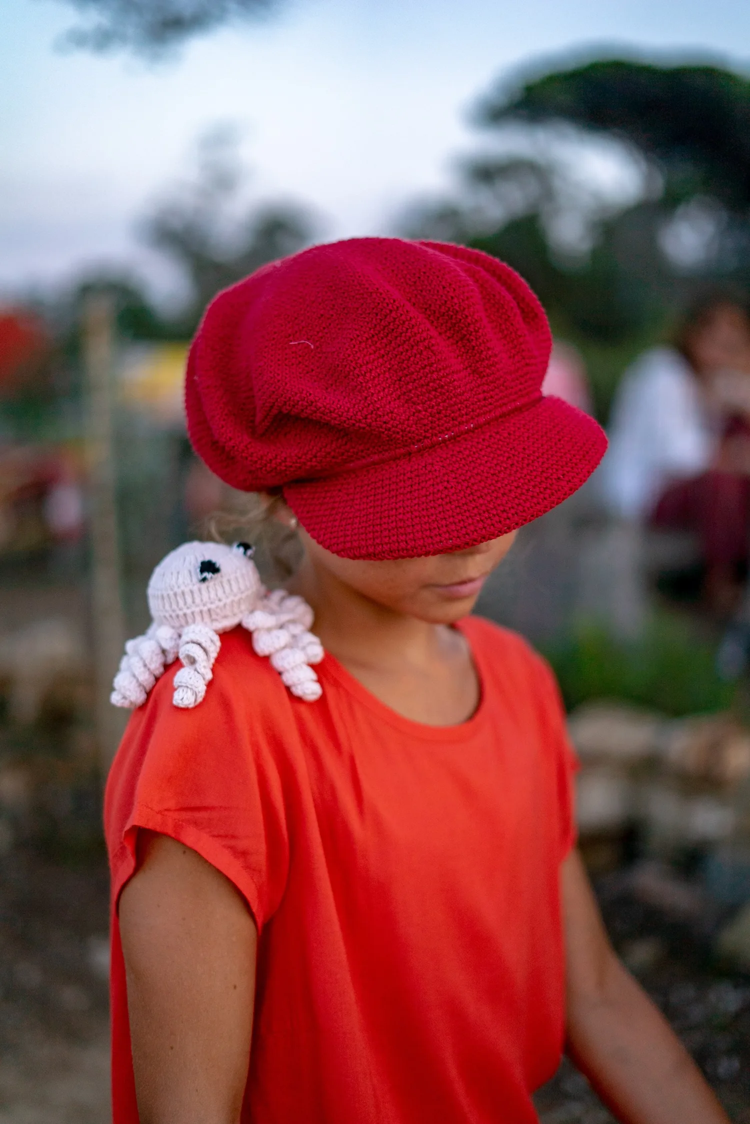 Enfant en casquette rouge crochet et tee-shirt orange, poulpe crocheté blanc sur l'épaule à Porquerolles.