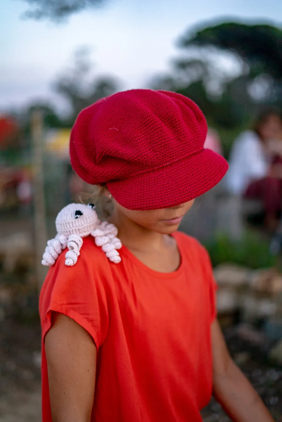 Enfant en casquette rouge crochet et tee-shirt orange, poulpe crocheté blanc sur l'épaule à Porquerolles.