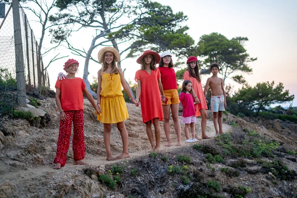 Sept enfants en tenues rouge, orange et jaune alignés sur un sentier côtier au crépuscule à Porquerolles.