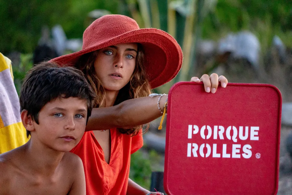 Fille en tunique et chapeau orange, panneau rouge PORQUEROLLES, garçon à ses côtés à Porquerolles.
