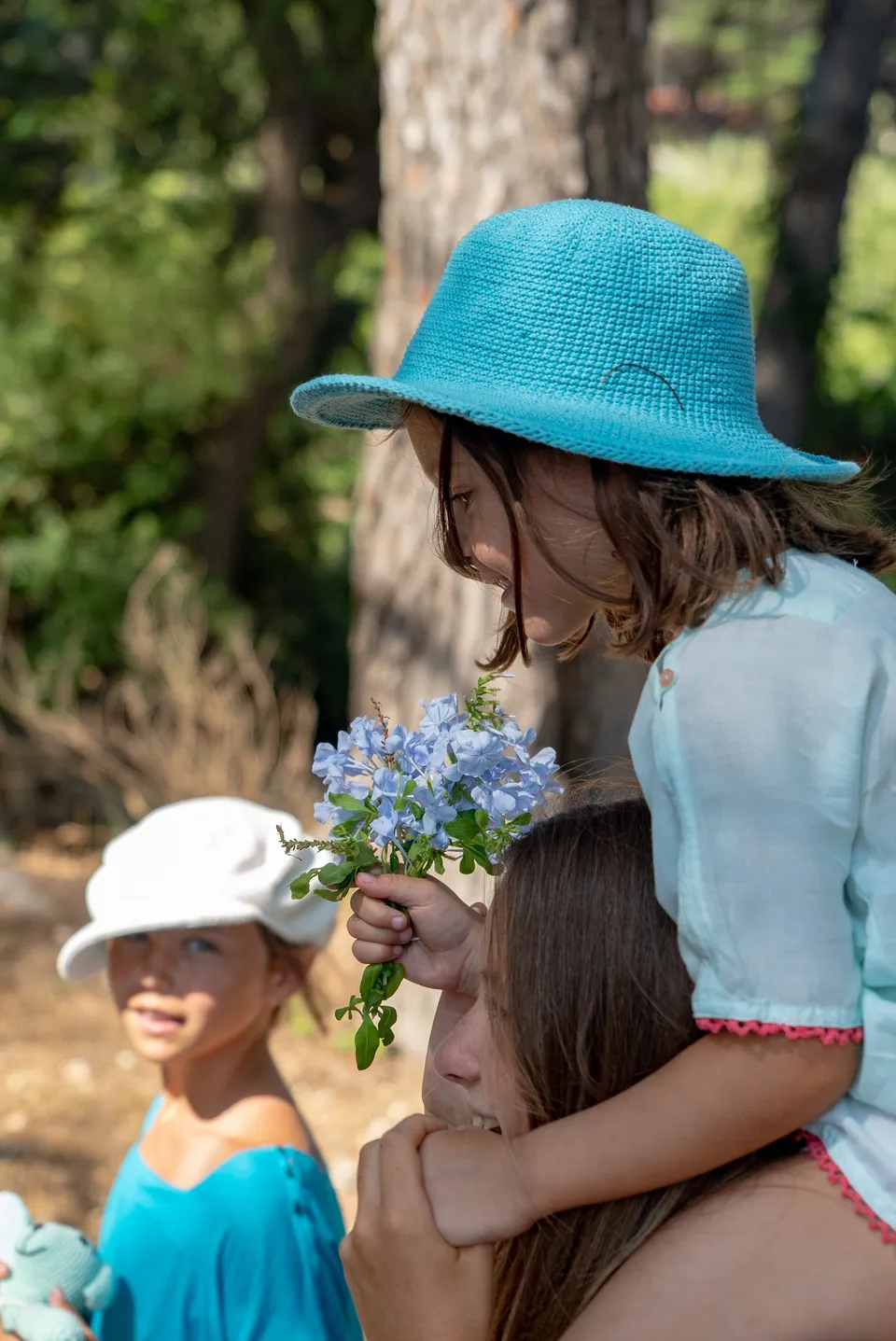 Petite fille au chapeau crochet turquoise sur les épaules d'une femme, bouquet de fleurs bleues à Porquerolles.