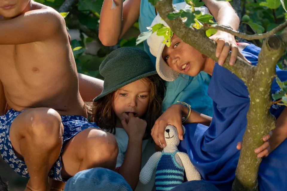 Enfants perchés dans un figuier, chapeaux de crochet et ours crocheté, lumière douce dans un jardin de Porquerolles.