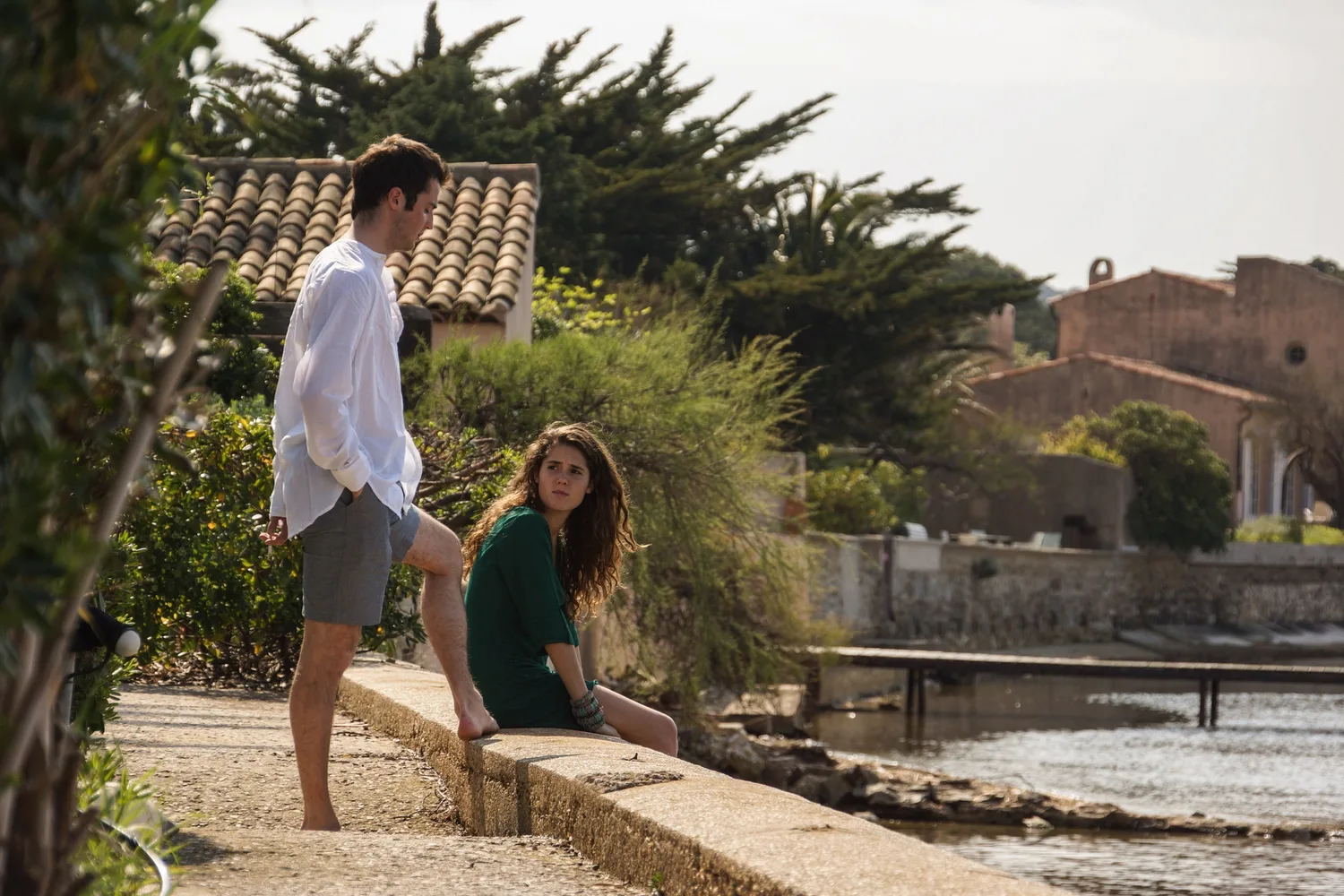 Un homme en chemise blanche et une femme en robe verte au bord de l’eau, devant les maisons du port.