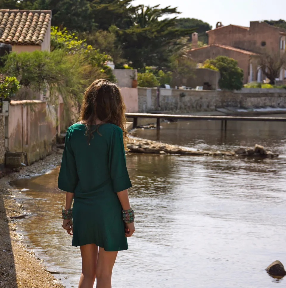 Femme de dos en robe verte au bord de l’eau devant les maisons du port.