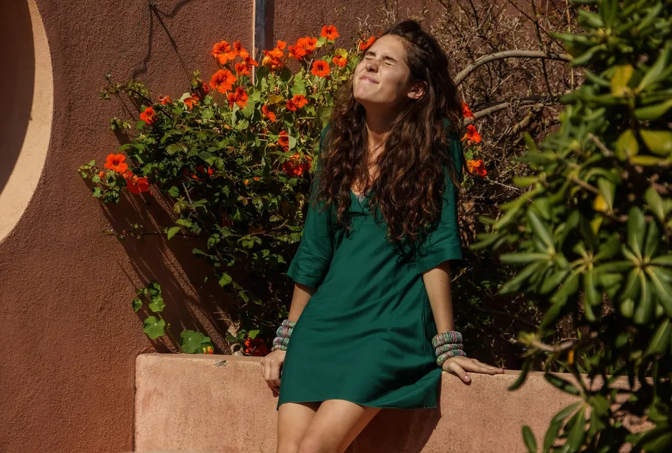 Femme en tunique grise et pantalon clair dans un jardin à Porquerolles.