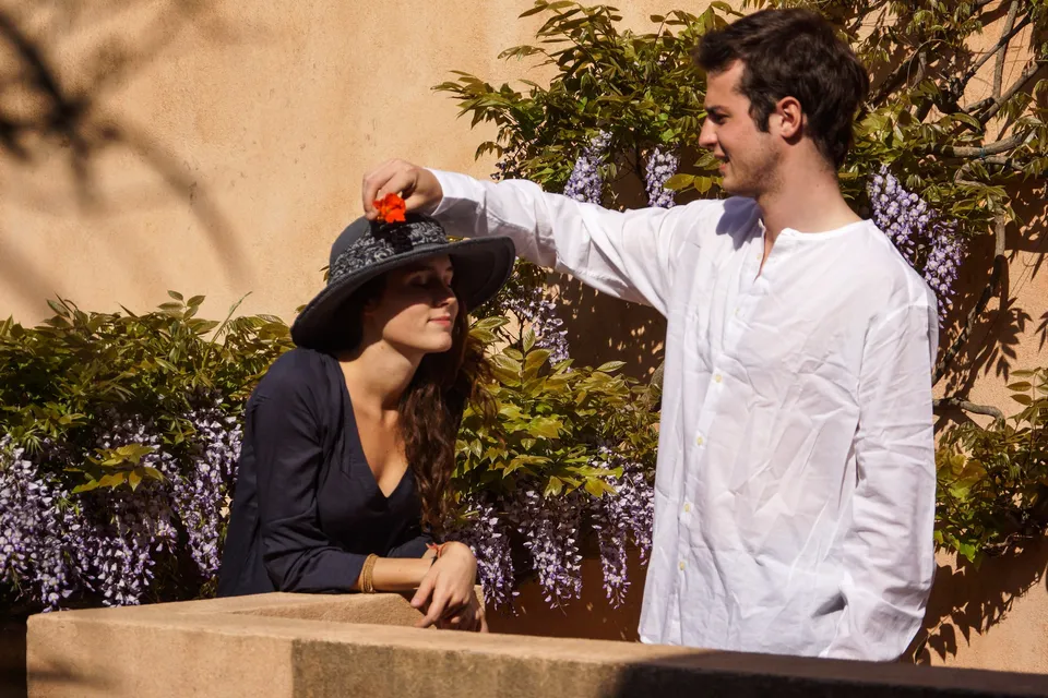 Homme ajustant le chapeau d’une femme en tunique devant une glycine à Porquerolles.
