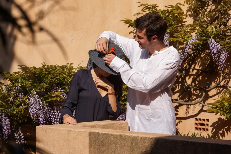 Homme ajustant le chapeau d’une femme en tunique devant une glycine à Porquerolles.