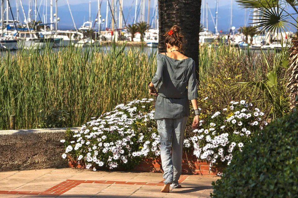 Femme en tunique grise et pantalon clair parmi les jardins de Porquerolles.