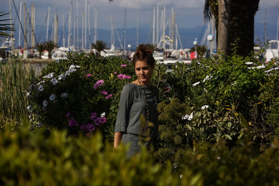 Femme en tunique grise et pantalon clair parmi les jardins de Porquerolles.