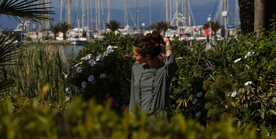 Femme en tunique grise et pantalon clair parmi les jardins de Porquerolles.